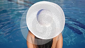 Fashion tanned female in white hat enjoying sunbathing near swimming pool back view close-up