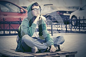 Fashion teen boy sitting on city sidewalk