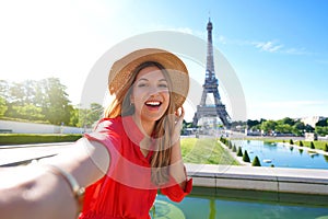 Fashion tourist woman with red dress and hat makes selfie photo with Eiffel Tower on the background in Paris, France. Concept