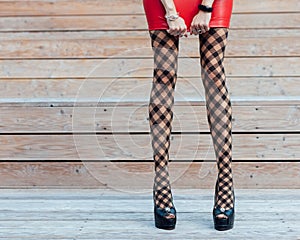 Fashion. A very girl with long legs in fashionable, fishnet stockings, a short red leather skirt and black high-heeled shoes
