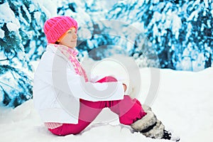 Fashion winter happy smiling woman sitting near branch christmas tree on snow wearing colorful knitted hat in snowy