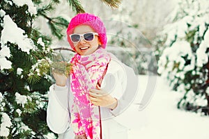 Fashion winter portrait happy smiling woman near branch christmas tree wearing colorful knitted hat in snowy