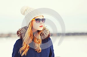 Fashion winter portrait pretty blonde woman wearing a jacket hat and sunglasses looks away over snowy