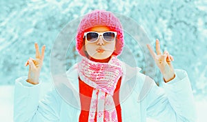 Fashion winter portrait of stylish young woman wearing sunglasses, colorful knitted hat and scarf in the park on snowy background