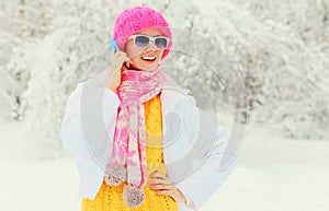 Fashion winter woman talking on smartphone wearing colorful knitted hat scarf over snowy background