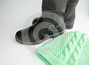 Fashion winter women`s shoes-black leather boots and knitted wool hat on a white background, the concept of buying warm clothes