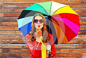 Fashion woman with colorful umbrella sends an air kiss in autumn