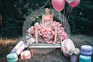 Fashion woman dressed in pink stunning dress surrounded of French Macarons