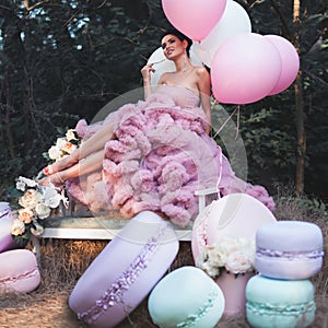 Fashion woman dressed in pink stunning dress surrounded of French Macarons