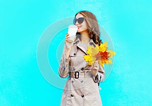 Fashion woman drinks coffee from cup holds autumn yellow maple leafs