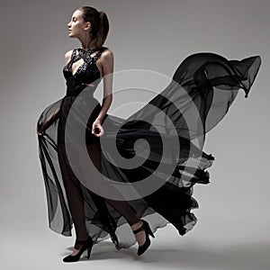 Fashion woman in fluttering black dress. Gray background.