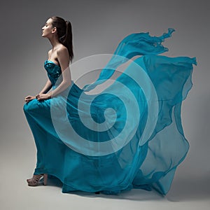 Fashion woman in fluttering blue dress. Gray background.