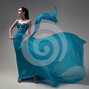 Fashion woman in fluttering blue dress. Gray background.