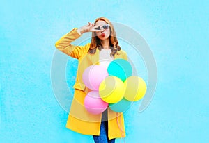 Fashion woman holds an air balloons in a yellow coat on colorful