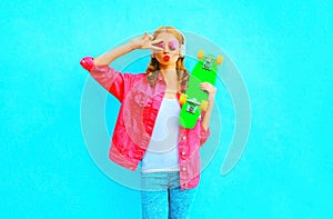 Fashion woman listens to music in a wireless headphones holds skateboard in a pink denim jacket