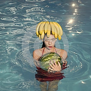 Fashion woman model posing. Girl on beach hold watermelon and banana in the blue pool. Tropical fruit diet. Summer