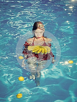 Fashion woman model posing. Vitamin in banana at girl sitting near water. woman with tropical fruit in pool. Woman relax