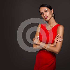 Fashion woman in red dress and bun hairstyle. Gold earrings. Dark background. Copycpase