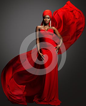 Fashion Woman in Red Dress and Hijab. African Model in Evening long Gown with flowing Silk Fabric over Dark Gray background.