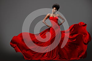 Fashion Woman in Red flying Dress with Afro Hairstyle. Dark Skinned Model in Silk Long Gown over Gray background. Happy elegant