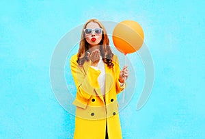 Fashion woman sends an air kiss holds balloon in a yellow coat