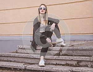 Fashion woman sitting on skateboard. Girl in sunglasses with longboard on stairs