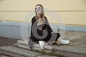 Fashion woman sitting on skateboard. Smiling Girl in sunglasses with longboard on stairs