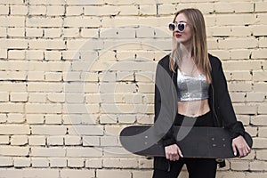 Fashion woman with a skateboard on brickwall background. Girl in sunglasses posing with longboard