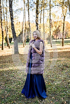 Fashion woman. Smiling girl in fur coat posin in autumn park with trees and ivy