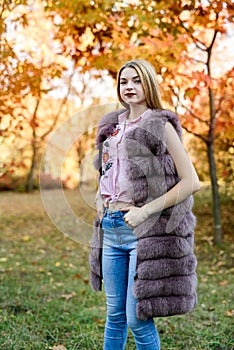 Fashion woman. Smiling girl in fur coat posin in autumn park with trees and ivy