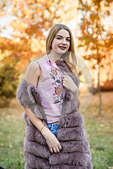 Fashion woman. Smiling girl in fur coat posin in autumn park with trees and ivy