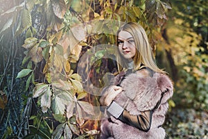 Fashion woman. Smiling girl in fur coat posin in autumn park with trees and ivy