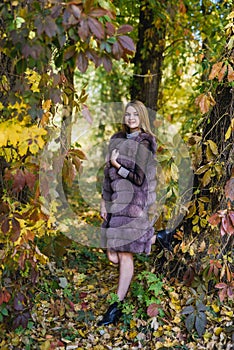 Fashion woman. Smiling girl in fur coat posin in autumn park with trees and ivy