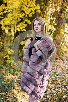 Fashion woman. Smiling girl in fur coat posin in autumn park with trees and ivy