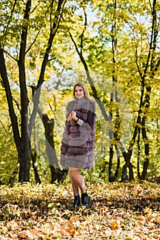 Fashion woman. Smiling girl in fur coat posin in autumn park with trees and ivy