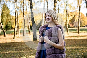 Fashion woman. Smiling girl in fur coat posin in autumn park with trees and ivy