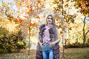 Fashion woman. Smiling girl in fur coat posin in autumn park with trees and ivy