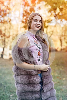 Fashion woman. Smiling girl in fur coat posin in autumn park with trees and ivy