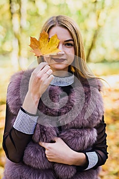 Fashion woman. Smiling girl in fur coat posin in autumn park with trees and ivy