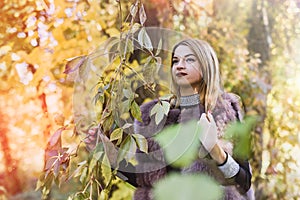 Fashion woman. Smiling girl in fur coat posin in autumn park with trees and ivy