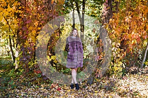 Fashion woman. Smiling girl in fur coat posin in autumn park with trees and ivy