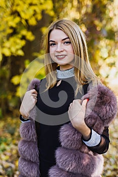 Fashion woman. Smiling girl in fur coat posin in autumn park with trees and ivy