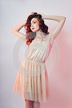 Fashion woman stands, bright red makeup, curly hair and light summer dress. Girl perfect art makeup colored background