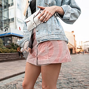 Fashion woman with stylish handbag in denim jacket and pink skirt walking in the city
