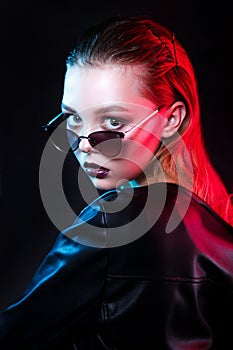 Fashion woman in stylish sungasses looking at camera over neon background