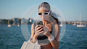 Fashion woman texting mobile phone on beautiful ocean waterfront close up.