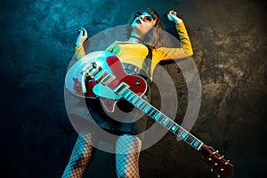 Fashion young hipster woman with curly hair with red guitar in neon lights. Rock musician is playing electrical guitar