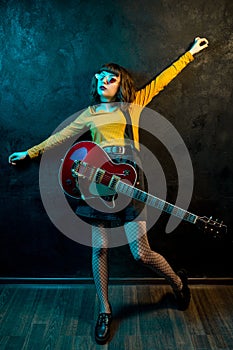 Fashion young hipster woman with curly hair with red guitar in neon lights. Rock musician is playing electrical guitar