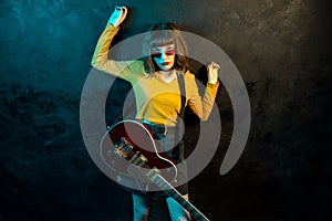 Fashion young hipster woman with curly hair with red guitar in neon lights. Rock musician is playing electrical guitar