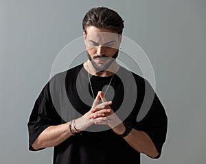 fashion young man with beard holding hands together and looking down